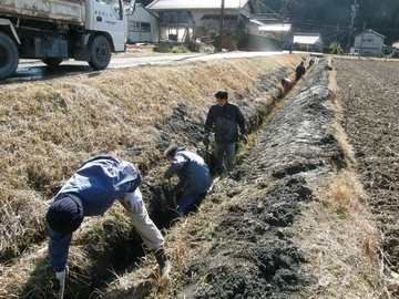溝さらいの様子の写真で、男性たちが溝の泥をすくっていて脇にはトラックが止まっている
