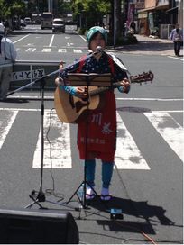 路上でギターの弾き語りする茶娘姿の女性