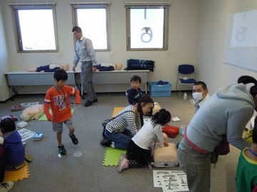 AED体験コーナーの写真。中央にはAEDを体験している親子やそれを見る子供の姿が写っている。