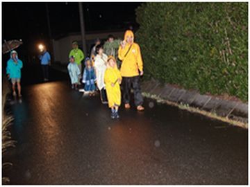 夜、雨が降る中、レインコートを着た小中学校の子どもたちが歩いている様子