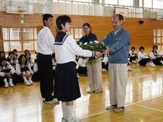 体育館で生徒を代表してサンパチェンスの苗を受け取る女子生徒と男子生徒