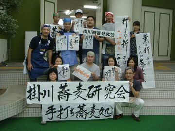 掛川蕎麦研究会手打ち蕎麦処と書かれた横断幕をなどを持つメンバーと参加者
