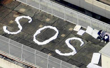 屋上に白い布でSOSの文字を書いた画像