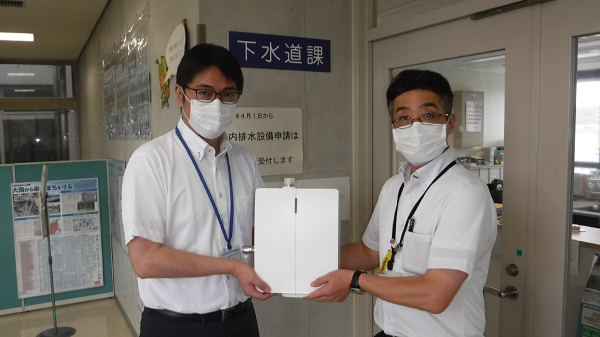 寄付されたオゾン水生成器を持つ男性2人の写真