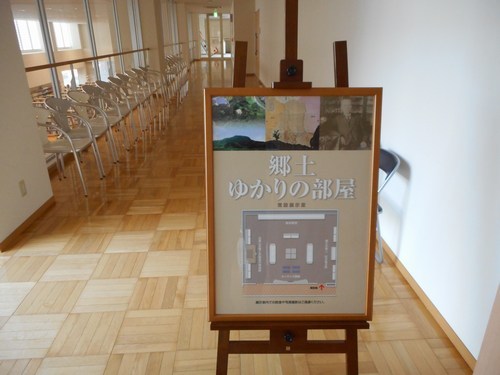 通路の一角に椅子が並べられ、手前に郷土ゆかりの部屋のポスターが置かれている写真。