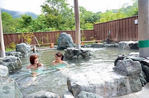 岩で囲まれた露天風呂に女性2人が入浴談笑している