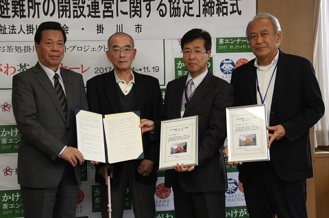松井市長と小野田理事長ら四人の男性が締結書を見せて並んでいる