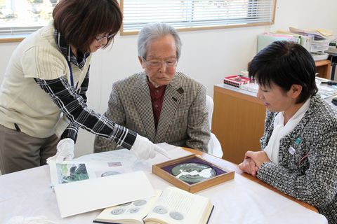 市学芸員から鏡の説明を受ける鈴木さんと山田教育長の写真