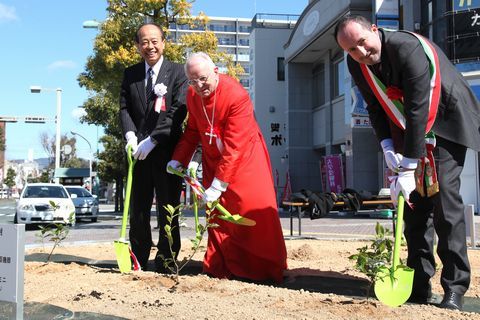 スコップを持ち笑顔で茶の苗木を植樹するモンテリーズィ枢機卿とヴィミニ副市長の写真
