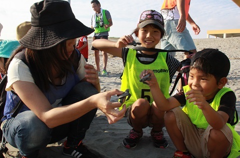 掛川総合スポーツクラブが主催するウミガメ放流体験にて、「アカウミガメ」の赤ちゃんと触れ合う家族