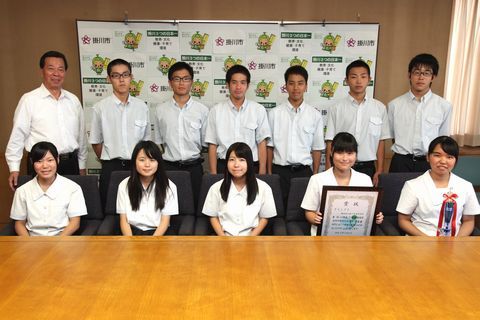 後列に全国大会に出場する男子高校生と松井市長が立ち、前列に女子高校生が座り、賞状とトロフィーを持っている写真