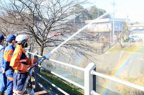消防団員と放水する水にかかる虹