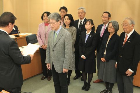 向かい合って立つ、9人の委員と書類を手に持つ松井市長