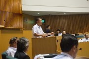 中央に議会室答弁席に立ち議会の仕組みを説明している市議会議員
