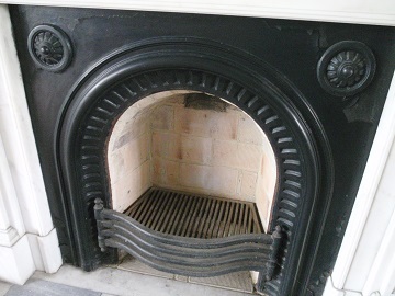 暖炉の炉の周辺写真。炉の周りは、四角い黒い鉄板で作られている。その鉄板にも、炉の入り口を囲うようにアーチ状に装飾されている。