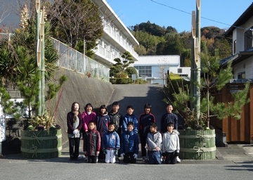 完成した一対のジャンボ門松の間で記念撮影する12人の児童と教職員ら