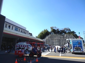 消防車や救急車の前に人が集まり、地震体験車による地震体験を行っている様子。