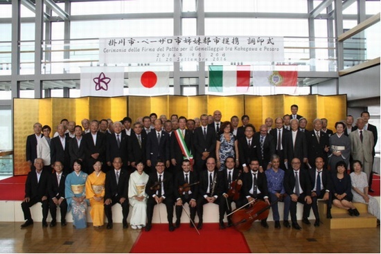 調印式の垂れ幕や国旗、金屏風の前で、正装の人たちが整列し、記念写真を撮っている様子。
