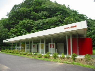 森を背景に、ねむの木こども美術館の白い屋根と赤や黄色の展示物が引き立つ自然豊かな場所の写真