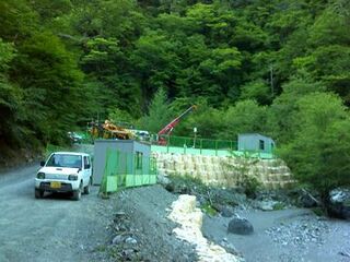 緑のフェンスで囲まれた奥で、クレーン車が作業している様子。