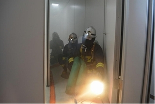 マスクを着けた消防隊員がライトをてらしながら、煙の充満した部屋から救助訓練する様子