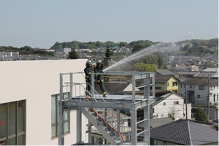 消防隊員二人が、消防署の高所から放水する様子