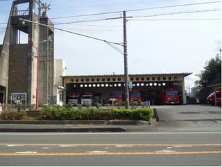 消防庁者全体を正面から見た画像。左にトレーニング用の塔があり、その横に救急車と消防自動車が並ぶ車庫