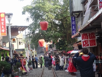 台湾の十份という町で赤い紙の熱気球を上げている様子。熱気球は道の真ん中の線路上で上げられていて、両サイドには商店などの建物が並び人が沢山集まっている
