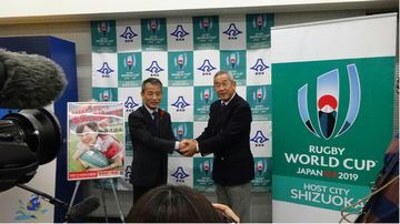 2人の男性が握手をする様子をたくさんの取材陣が撮影する様子
