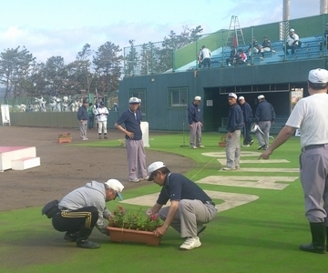野球場。何人もの大人の男の人が開会式の準備をしている