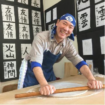 楽しそうに蕎麦をのし棒で伸ばしている様子の写真