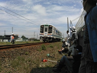 電車が走る姿を線路脇から間近に見る草刈りの人たち