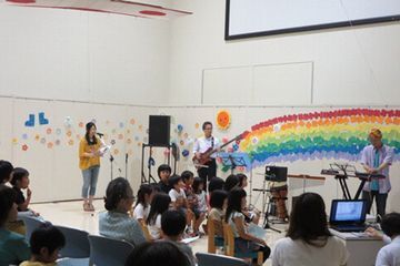 壁に虹や花の飾りつけをしたステージに地元の音楽家が聞きに来た親子連れに披露している様子