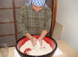 バンダナをまいた男性がそば粉を練っている画像
