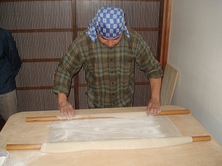 バンダナをまいた男性がのし棒を使ってそばの生地を伸ばしている画像