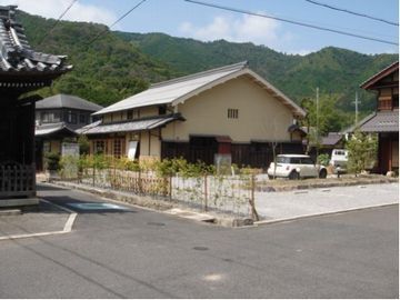 交差点の奥に平屋の建物手前に駐車場がある