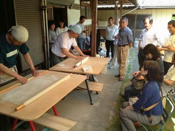 そば打ちを披露する人とその様子を楽しむ参加者たち