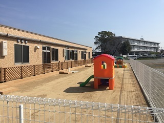 すずかけっこ保育園（鳥居町）のフェンスで囲われた園庭。手前にオレンジ色の遊具がある写真