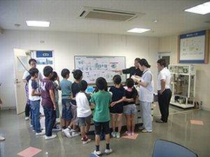 市内小学生が見学時にホワイトボードの前で説明を受けている様子