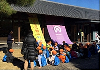 二の丸美術館の前で子どもたちが座って話を聞いている写真
