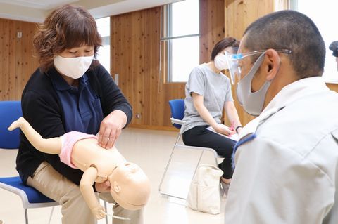 こどもの人形の胸を抑える園の職員と指導する消防署員