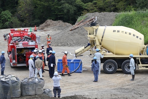 ミキサー車から大きな容器に水を入れ、そこに消防車のホースで水を補給している