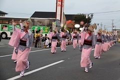 着物と笠を身につけた女性が阿波踊りを踊る一行とそれを見物する人々