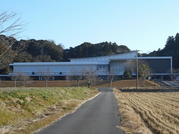 図書館の建物全体を正面から撮った写真。手前には図書館に続く道や、田んぼが写っている。
