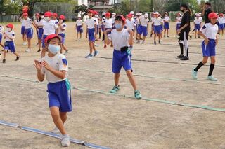 運動場にて、地面に並べた一人一本のロープを跨いだり、ロープの上をバランスを取りながら歩く児童の様子