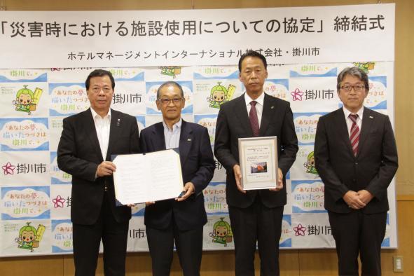 災害時における施設使用についての協定、締結式のパネルの前で、認定書等締結した書面を並んで掲げている松井市長と3人の男性関係者の記念写真
