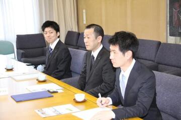 協定締結式で3人の男性が話している様子