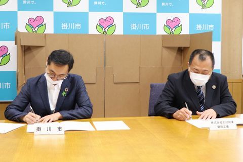 協定書にサインする立田工場長(右)と久保田市長