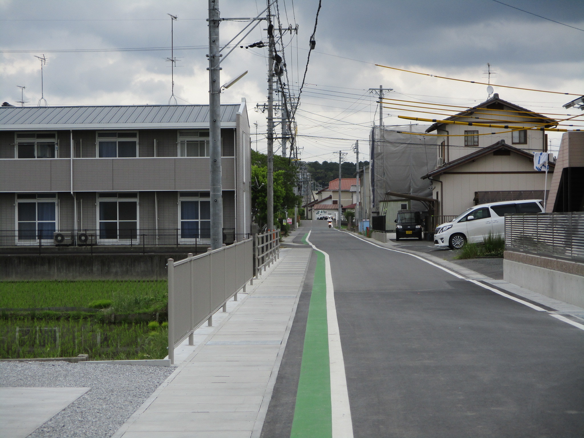 市道「一ノ坪二ノ坪線（大池地内）」施工後の道路、道路の道幅が広がっているが歩道と車道が区分されていないためグリーンベルトで歩道部分を確保している