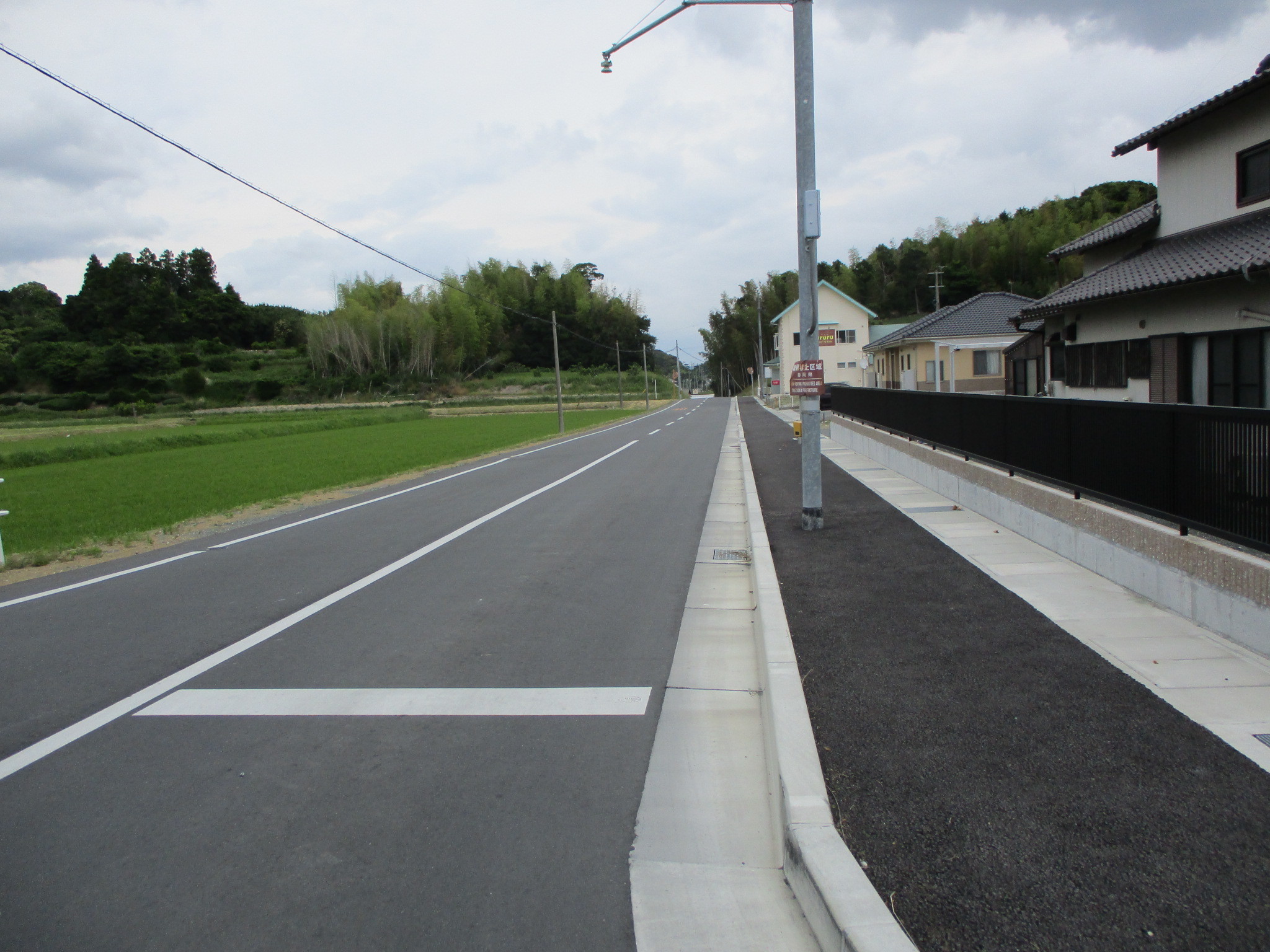 市道「川久保釜田線（三井地内）」施工後の道路、歩道部分が分離され、縁石で境目が作られた。透水性舗装がされた道路に施工された